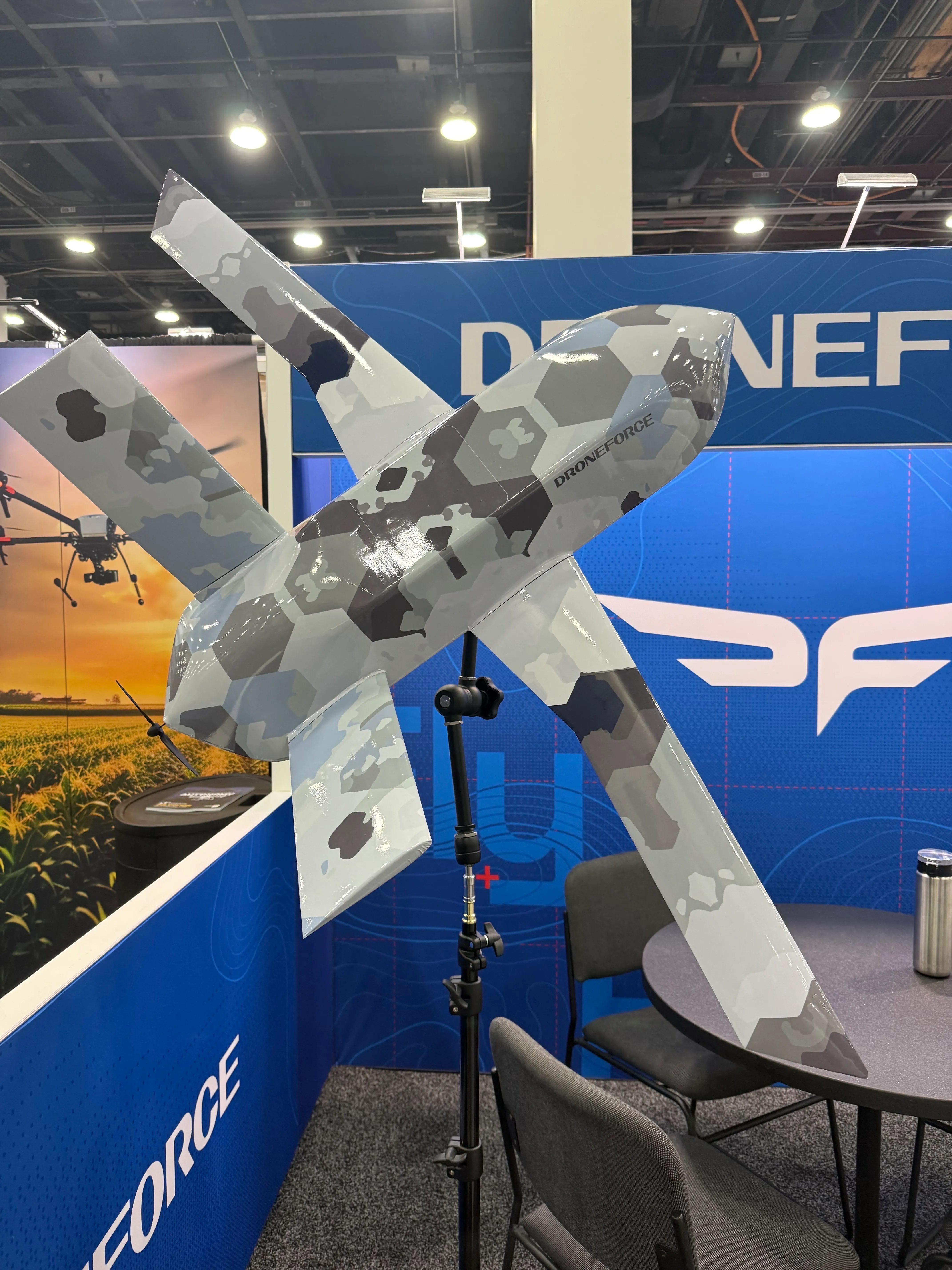 A hexagon-camouflaged Droneforce fixed-wing aircraft mounted on a display stand.